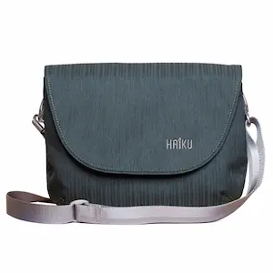 Dark teal crossbody bag with a rounded flap closure and a light gray adjustable shoulder strap. The compact bag has subtle vertical texture and the Haiku logo printed on the front.