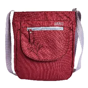 Red textured crossbody bag with a light gray adjustable shoulder strap and a rounded front pocket. A horizontal silver zipper sits above the front pouch with a small matching pull tab.