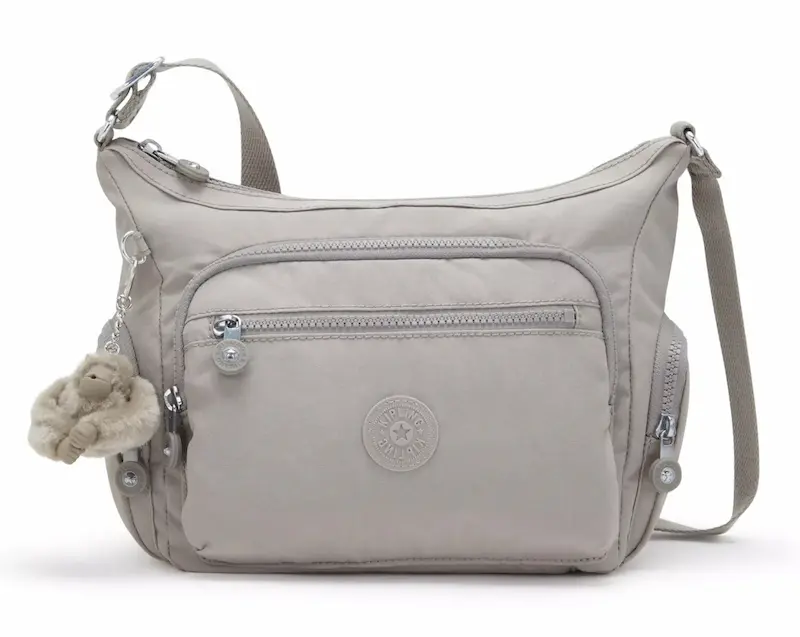 Light gray crossbody bag with an adjustable shoulder strap and several zippered compartments. The front has a large rectangular pocket with a smaller horizontal zipper above it and a plush monkey charm hanging from the side.