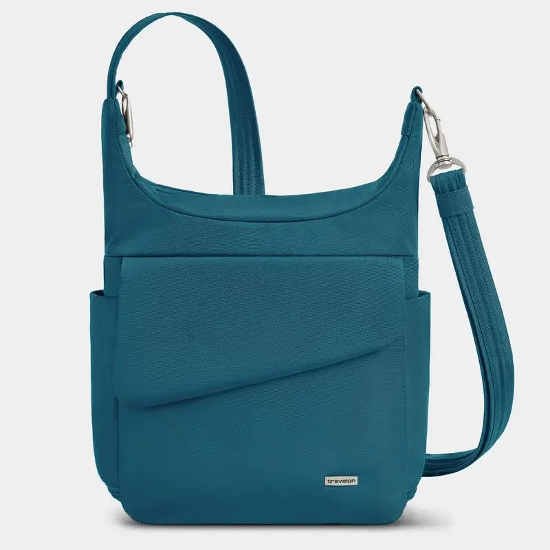 Teal crossbody travel bag with a short top handle and a long detachable shoulder strap with silver clips. The rectangular bag has a large angled front pocket and slim side pockets.
